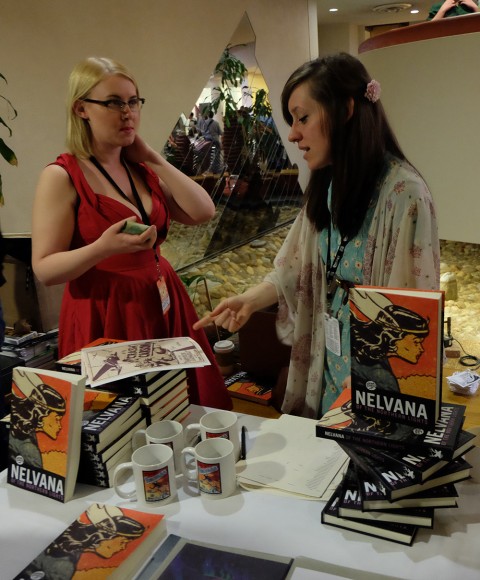 Rachel Richey admires her Jack Tremblay signed page while Hope Nicholson looks on at their Nelvana reprint book table.